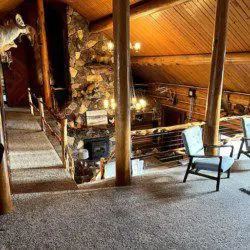 Wooden lodge interior with loft seating, stone fireplace, and taxidermy decor in Fairbanks, Alaska