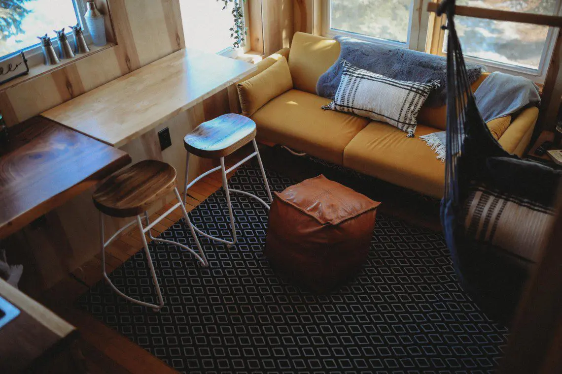 Small sitting area with yellow couch, stools, and pouf in a sunlit Fairbanks Alaska treehouse