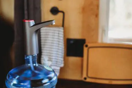 Water jug with dispenser on counter near sink and utensils in a Fairbanks Alaska treehouse