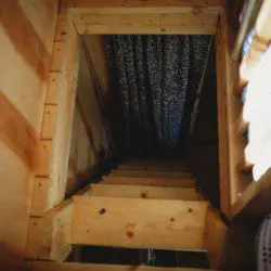 Rustic wooden staircase leading to a loft area, framed with pine walls and patterned curtains in a Fairbanks Alaska treehouse