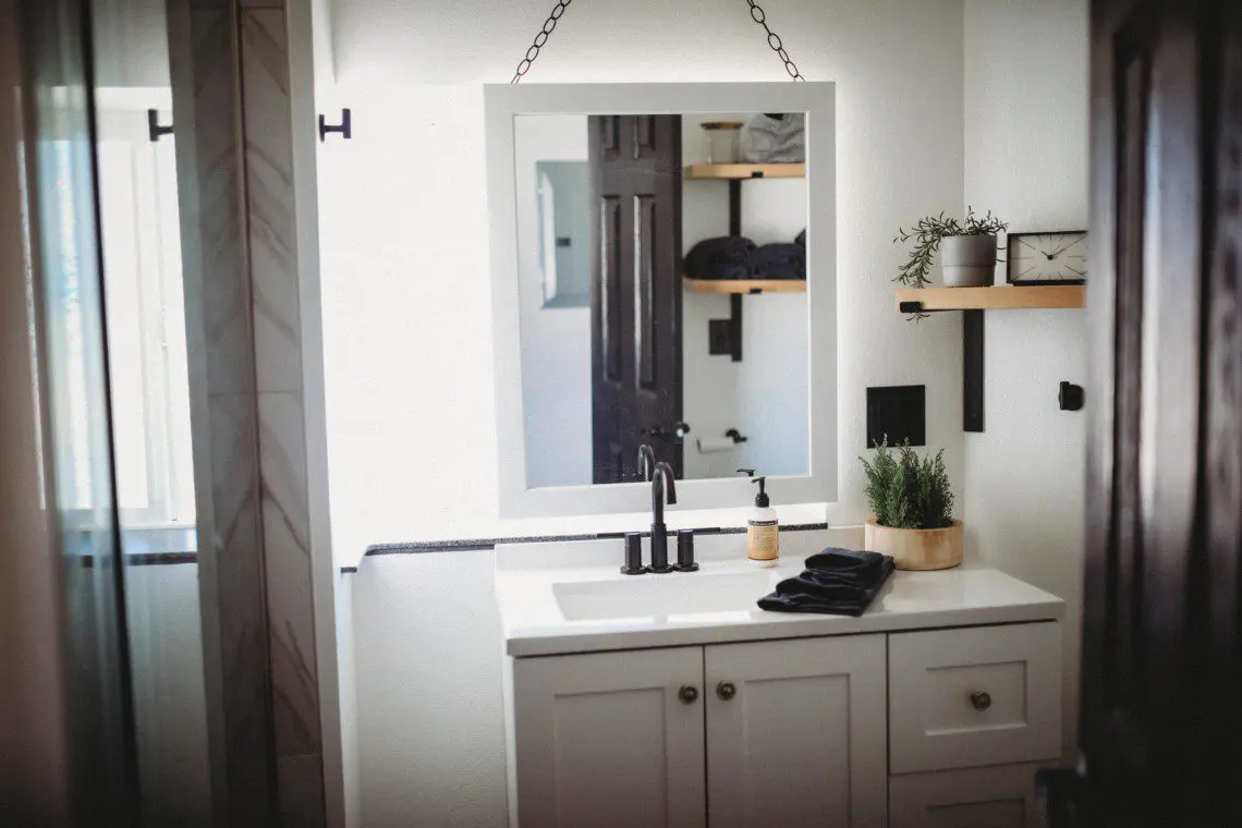 White vanity with square mirror, black faucet, and decorative shelves in a bright Fairbanks Alaska treehouse bathroom