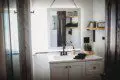 White vanity with square mirror, black faucet, and decorative shelves in a bright Fairbanks Alaska treehouse bathroom