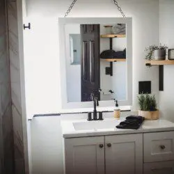 White vanity with square mirror, black faucet, and decorative shelves in a bright Fairbanks Alaska treehouse bathroom