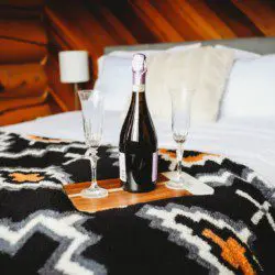 Bottle of champagne and glasses on bed with patterned blanket in cozy Fairbanks treehouse rental