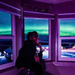 Person watching northern lights through large windows inside a Fairbanks Alaska treehouse rental