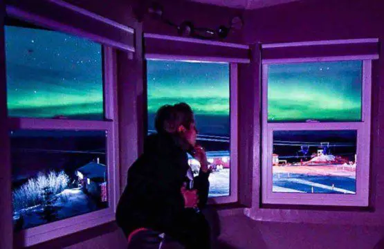 Person watching northern lights through large windows inside a Fairbanks Alaska treehouse rental