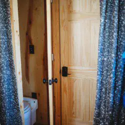 Wood-paneled bathroom with curtain doorway and view of toilet in a cozy Fairbanks Alaska treehouse rental