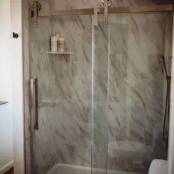 Glass-enclosed shower with marble-style walls in a Fairbanks Alaska treehouse bathroom