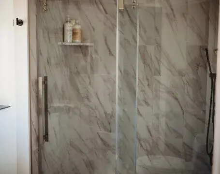 Glass-enclosed shower with marble-style walls in a Fairbanks Alaska treehouse bathroom