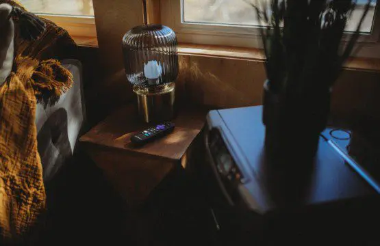 Wooden side table with lamp and remote beside a window in a warm Fairbanks Alaska treehouse interior