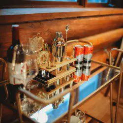 Gold bar cart with wine, glasses, and cocktail tools in a log-walled Fairbanks Alaska treehouse rental