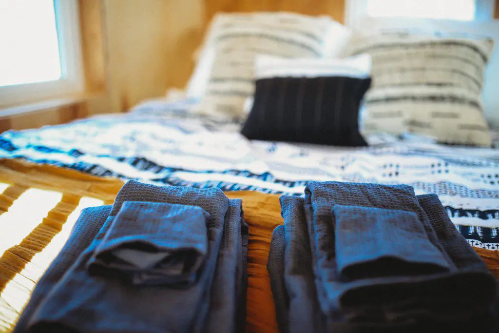 Folded dark towels on a wooden bench in front of a cozy bed with patterned pillows in a Fairbanks Alaska treehouse rental