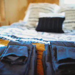 Folded dark towels on a wooden bench in front of a cozy bed with patterned pillows in a Fairbanks Alaska treehouse rental