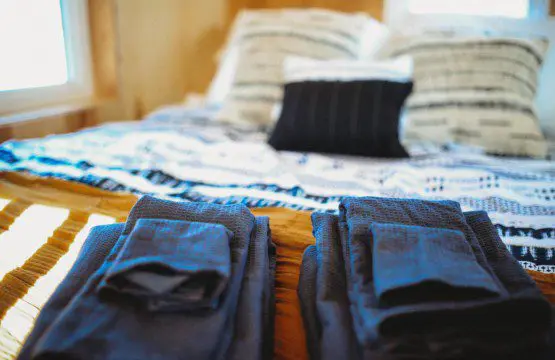 Folded dark towels on a wooden bench in front of a cozy bed with patterned pillows in a Fairbanks Alaska treehouse rental