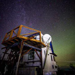 Unique wooden lodge structure with elevated deck beneath a brilliant night sky and stars in Fairbanks, Alaska