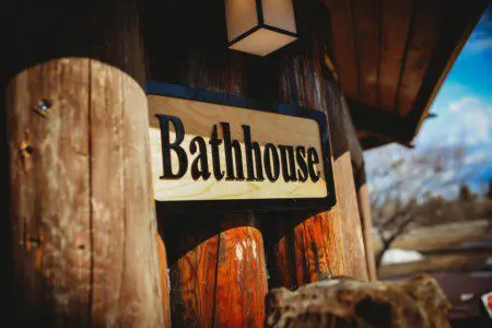 Wooden bathhouse sign mounted on log wall at Fairbanks Alaska lodge with carved bear sculpture