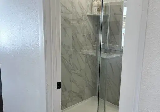 Glass-enclosed shower with marble-style tile in a modern Fairbanks treehouse bathroom