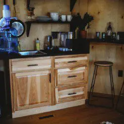 Rustic kitchen with water dispenser, hanging pans, and open shelving in a Fairbanks Alaska treehouse rental