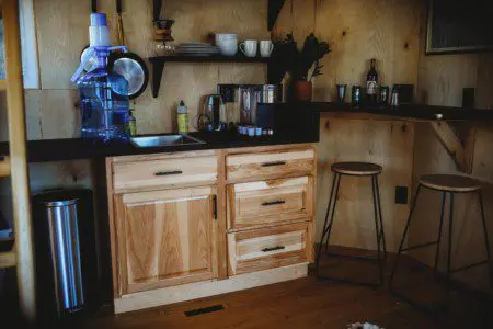 Rustic kitchen with water dispenser, hanging pans, and open shelving in a Fairbanks Alaska treehouse rental