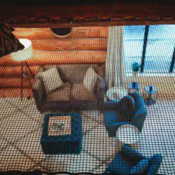 View through mesh of a log cabin-style sitting area with couch, chairs, and large windows in Fairbanks Alaska