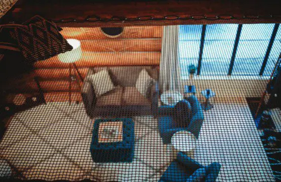 View through mesh of a log cabin-style sitting area with couch, chairs, and large windows in Fairbanks Alaska