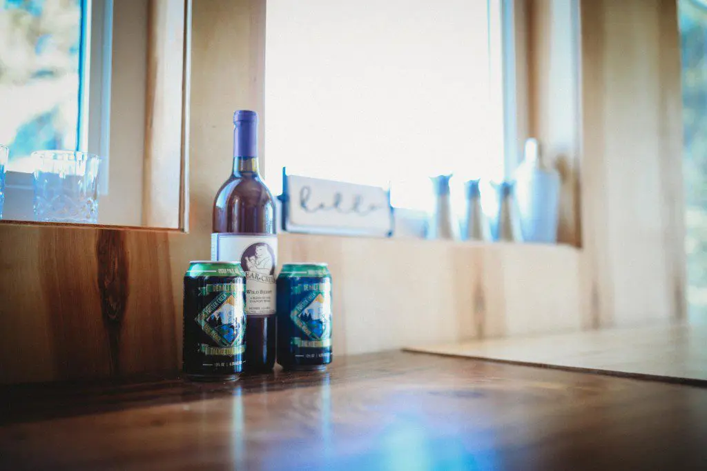 Wine bottle and canned drinks on wooden counter near window in a Fairbanks Alaska treehouse rental