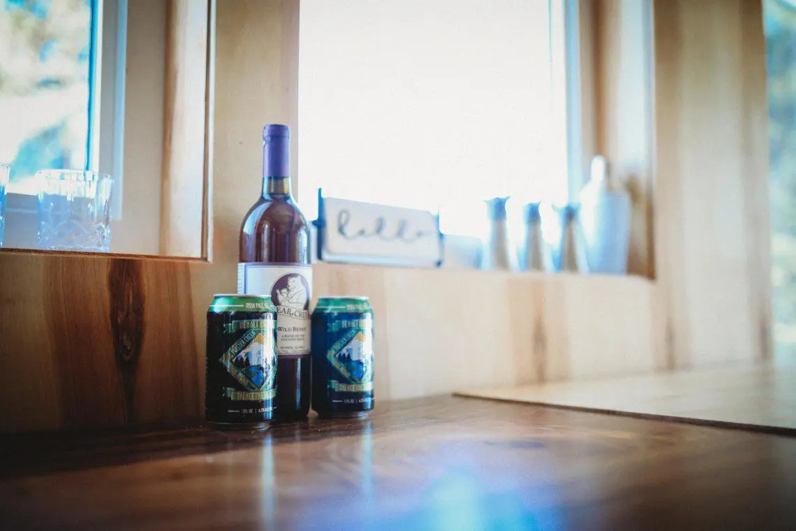 Wine bottle and canned drinks on wooden counter near window in a Fairbanks Alaska treehouse rental