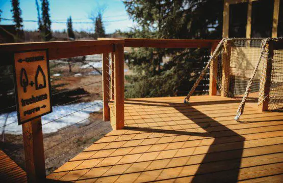 Wooden treehouse cabin with rope bridge entrance nestled in pine forest near Fairbanks, Alaska