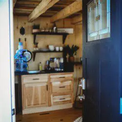 Open front door revealing cozy kitchenette with wooden cabinets and black countertop in a Fairbanks Alaska treehouse rental