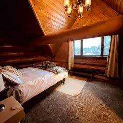 Cozy loft-style bedroom with wood-paneled walls and large window in Fairbanks Alaska treehouse