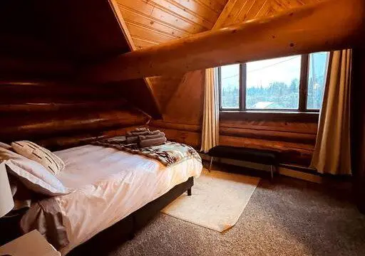 Cozy loft-style bedroom with wood-paneled walls and large window in Fairbanks Alaska treehouse