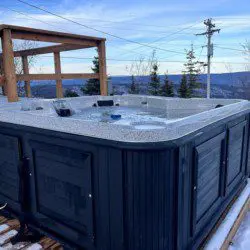 Outdoor hot tub filled with water surrounded by snow and overlooking a forested landscape in Fairbanks, Alaska