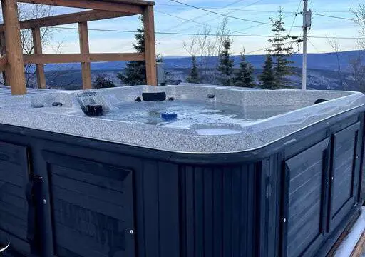 Outdoor hot tub filled with water surrounded by snow and overlooking a forested landscape in Fairbanks, Alaska