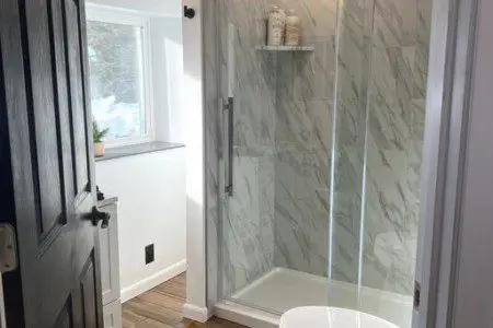 Bright bathroom with glass shower, wood floors, and white walls in a Fairbanks treehouse rental