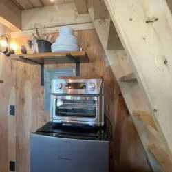 Small oven on mini fridge with wooden stairs and shelving in a rustic Fairbanks Alaska treehouse
