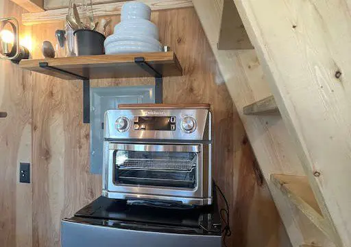 Small oven on mini fridge with wooden stairs and shelving in a rustic Fairbanks Alaska treehouse