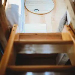 Wooden ladder leading to loft beside windows and kitchenette in Fairbanks Alaska treehouse