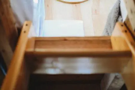 Wooden ladder leading to loft beside windows and kitchenette in Fairbanks Alaska treehouse