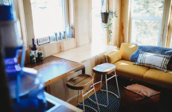 Cozy sitting area with stools, yellow sofa, and wood accents in a Fairbanks Alaska treehouse rental
