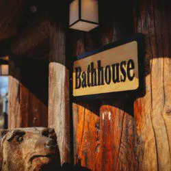 Wooden bathhouse sign mounted on log wall at Fairbanks Alaska lodge with carved bear sculpture