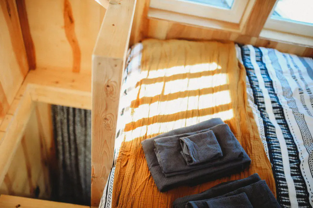 Sunlit wooden bed with folded towels and blankets in a Fairbanks Alaska treehouse rental