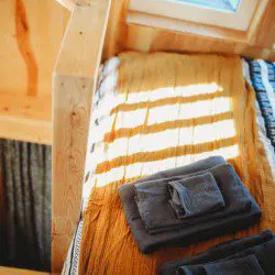 Sunlit wooden bed with folded towels and blankets in a Fairbanks Alaska treehouse rental