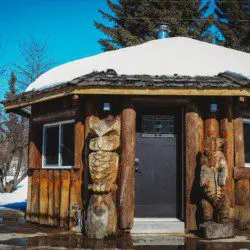 Round log cabin bathhouse with owl and bear wood carvings in snowy Fairbanks Alaska setting