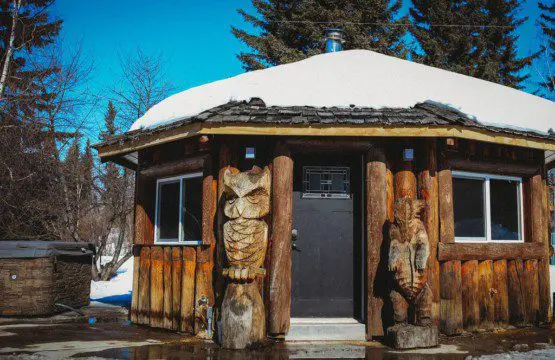 Round log cabin bathhouse with owl and bear wood carvings in snowy Fairbanks Alaska setting