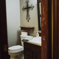 Cozy bathroom with wooden vanity, wall cross decor, and toilet in a Fairbanks Alaska lodge or treehouse rental