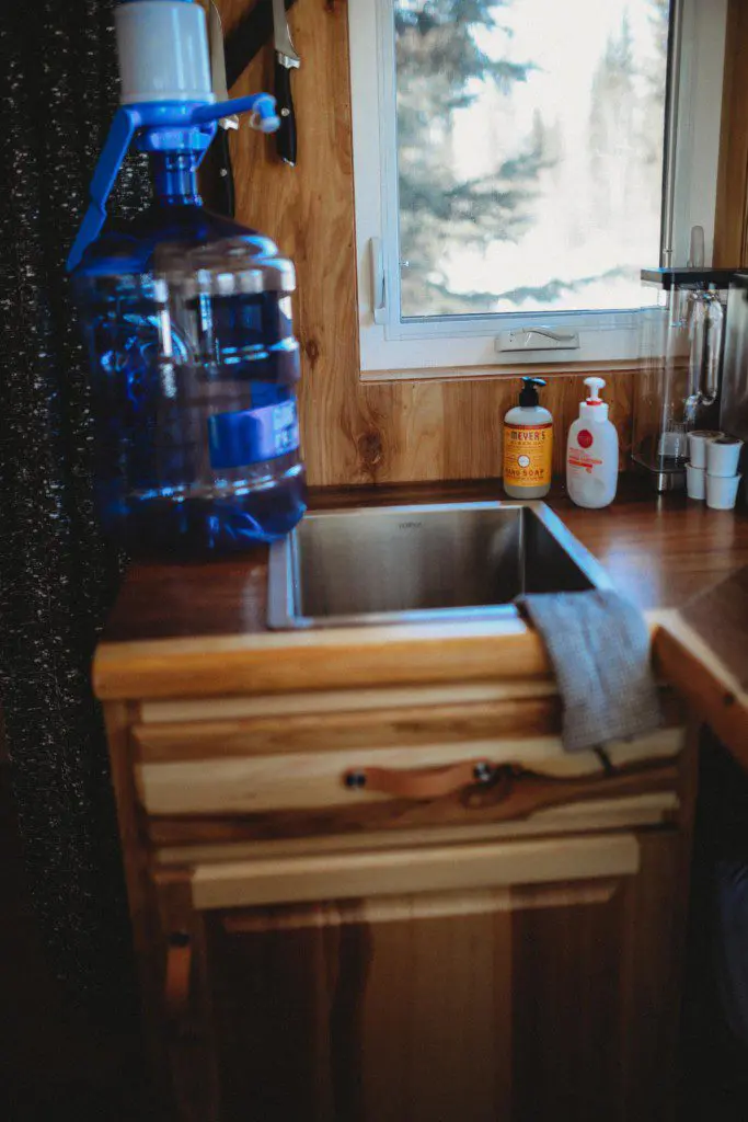 Compact wooden sink station with water jug and supplies in a Fairbanks Alaska treehouse rental