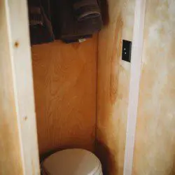 Small wooden bathroom with toilet and hanging towels in a Fairbanks Alaska treehouse