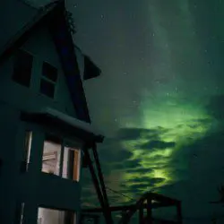 Northern lights glowing above a Fairbanks treehouse-style lodge at night