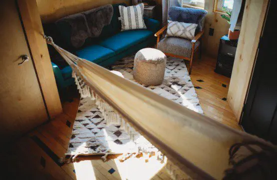 Inviting Fairbanks treehouse interior with hammock, teal sofa, cozy rug, and natural wood decor