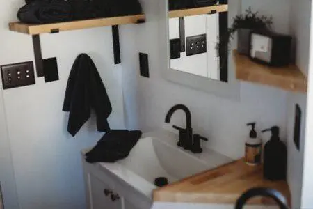 Compact modern bathroom with dual sinks, wood shelves, and black fixtures in Fairbanks Alaska rental